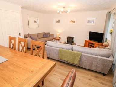 A living room with two sofas a wooden dining table chairs a television and a small stove at 4 Ty Rhosyn in Morfa Bychan