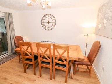 A dining room with a wooden table surrounded by six chairs a wall clock and a floor lamp at 4 Ty Rhosyn Morfa Bychan