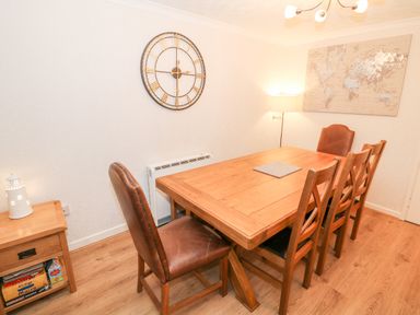 A dining room with a wooden table and six chairs including two leather chairs a large wall clock a floor lamp and a wall map at 4 Ty Rhosyn Morfa Bychan
