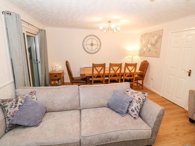 A living area with a gray sofa and a wooden dining table with chairs at 4 Ty Rhosyn in Morfa Bychan