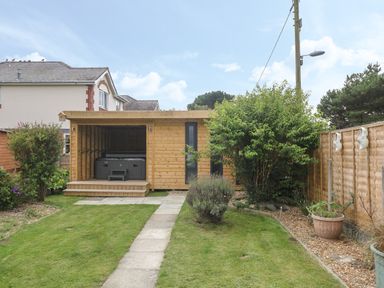 A backyard with a wooden shed housing a hot tub beside a lawn and garden at 4 Ty Rhosyn Morfa Bychan