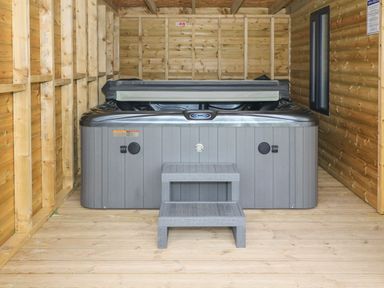 A hot tub with steps inside a wooden enclosure at 4 Ty Rhosyn in Morfa Bychan