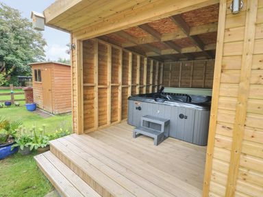 A wooden outdoor shelter with a hot tub and steps in a garden at 4 Ty Rhosyn in Morfa Bychan