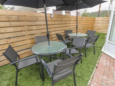 An outdoor seating area with two round glass tables and black chairs on artificial grass at 4 Ty Rhosyn in Morfa Bychan