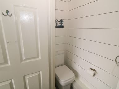 A small bathroom with a white toilet and a toilet roll holder on a shiplap wall at 4 Ty Rhosyn in Morfa Bychan