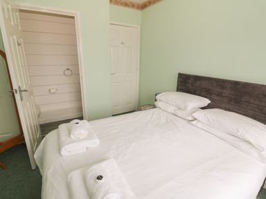 A bedroom with a double bed white linens and towels and partially open doors leading to a bathroom and a closet at 4 Ty Rhosyn in Morfa Bychan