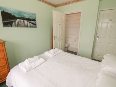 A bedroom with a bed with folded towels on top a wooden dresser a partially open door leading to a bathroom at 4 Ty Rhosyn in Morfa Bychan