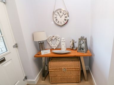 An entryway table with a lamp heart decoration lighthouse anchor lantern key box under a wall clock and a wicker storage basket at Driftwood Haven in Carbis Bay