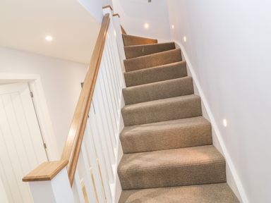 A carpeted staircase with wooden handrail and white balusters in a hallway at Driftwood Haven in Carbis Bay