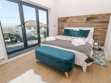 A bedroom with a bed, teal bench, large window, and wooden floor at Driftwood Haven in Carbis Bay