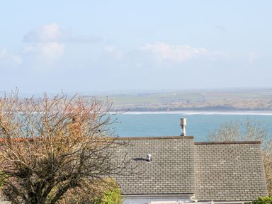 A view of rooftops and trees with the sea and hills in the background at Driftwood Haven in Carbis Bay
