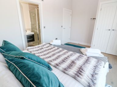 A bedroom with teal pillows on the bed and a bathroom visible through an open door at Driftwood Haven in Carbis Bay
