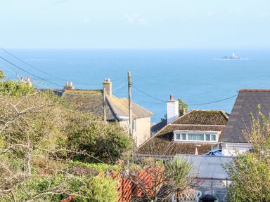 Houses with rooftops and chimneys overlooking the sea with a small island and lighthouse in the distance at Driftwood Haven in Carbis Bay