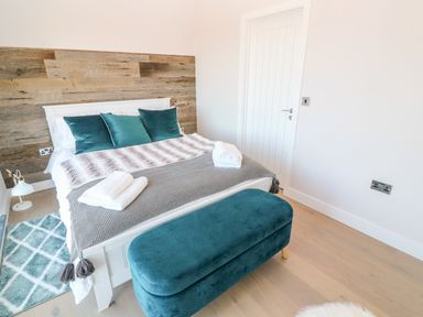 A bedroom with a white bed frame blue cushions blue ottoman and patterned rug at Driftwood Haven in Carbis Bay
