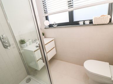 A bathroom with a shower enclosure a white vanity unit a toilet and a window with blinds at Driftwood Haven in Carbis Bay