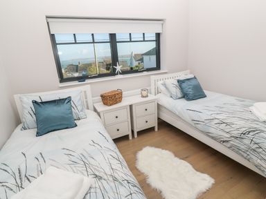 A bedroom with two single beds blue patterned bedding a small white rug and a window with a sea view at Driftwood Haven in Carbis Bay