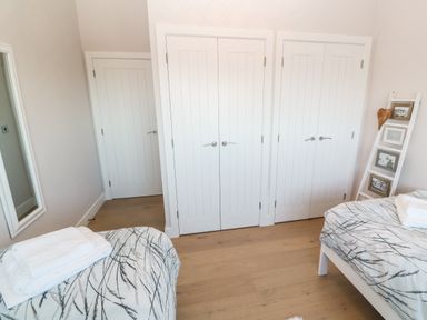 A bedroom with two beds with patterned bedding wooden floor white doors and a ladder shelf with photos at Driftwood Haven in Carbis Bay