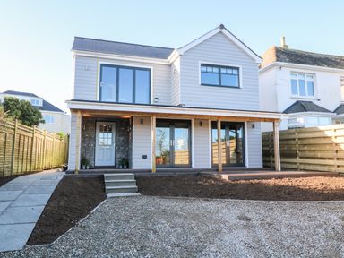 A two-story house with a covered porch a gravel driveway and fenced garden at Driftwood Haven in Carbis Bay