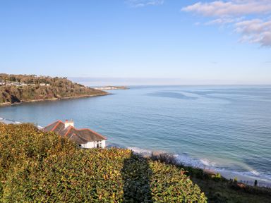 A coastal view with a house near the shoreline and a bay with hills in the background at Driftwood Haven in Carbis Bay