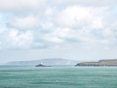 A seascape with a small island with a lighthouse in the water and cliffs in the background at Driftwood Haven in Carbis Bay