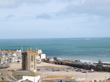 A coastal town with a stone church tower boats on the beach and the sea in the background at Driftwood Haven in Carbis Bay