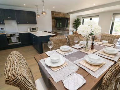 A dining table with place settings and a flower vase in an open kitchen and living area at Driftwood Haven in Carbis Bay