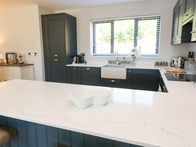 A kitchen with dark cabinets a white countertop a white sink a window with blinds and a white bowl on the island at Driftwood Haven in Carbis Bay