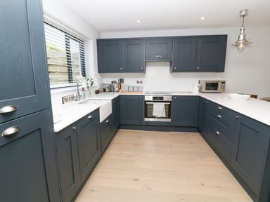 A kitchen with dark cabinets a white countertop and wooden floor at Driftwood Haven in Carbis Bay