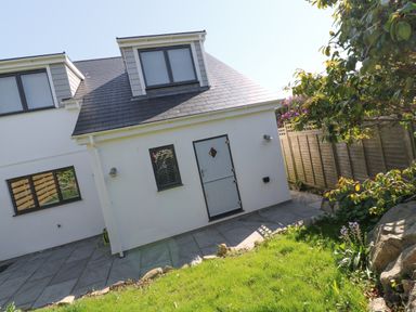 A back view of a house with two windows a door a paved patio and a garden with grass and plants at Driftwood Haven in Carbis Bay
