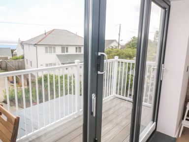A sliding glass door opening to a balcony with white railing and wooden floorboards overlooking neighboring houses at Driftwood Haven in Carbis Bay