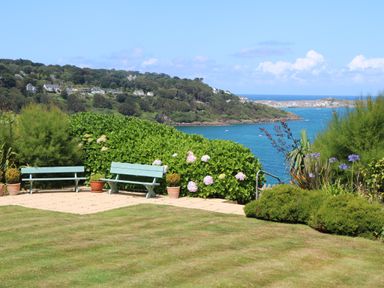 A garden with two blue benches and potted plants overlooking a body of water with hills and houses in the background at Meridian Carbis Bay