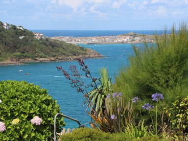 A coastal view with blue water boats green bushes and purple flowers at Meridian in Carbis Bay