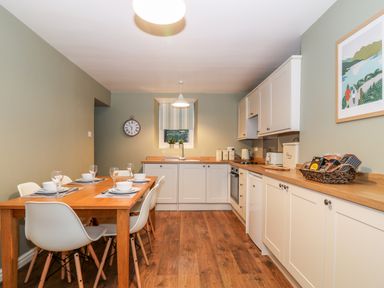 A kitchen with wooden floor white cabinets and a wooden dining table set for six at Yr Hen Dy Capel in Blaenau Ffestiniog