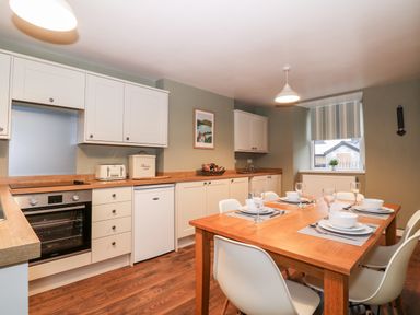 A kitchen with white cabinets wooden countertops and a wooden dining table set for four at Yr Hen Dy Capel in Blaenau Ffestiniog