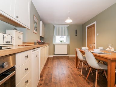 A kitchen with wooden floor white cabinets a wooden dining table and white chairs at Yr Hen Dy Capel in Blaenau Ffestiniog