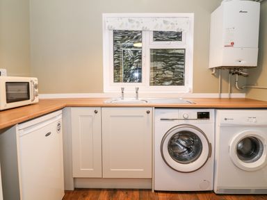 A utility room with a washing machine dishwasher sink microwave and boiler at Yr Hen Dy Capel in Blaenau Ffestiniog