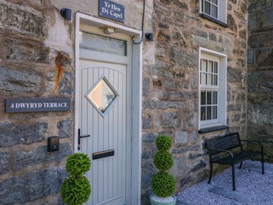 The stone exterior of a building with a white door and a bench outside at Yr Hen Dy Capel in Blaenau Ffestiniog