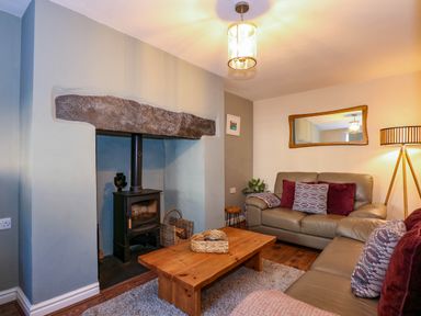 A living room with leather sofas a wooden coffee table a wood burning stove and a floor lamp at Yr Hen Dy Capel in Blaenau Ffestiniog