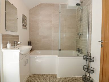 A bathroom with a white sink cabinet a bathtub with shower and glass screen and wall tiles in Yr Hen Dy Capel in Blaenau Ffestiniog
