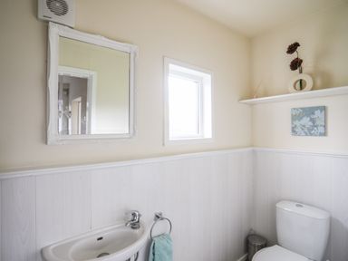 A small bathroom with a sink toilet white paneled walls and a window at Glyn Morfa in Harlech