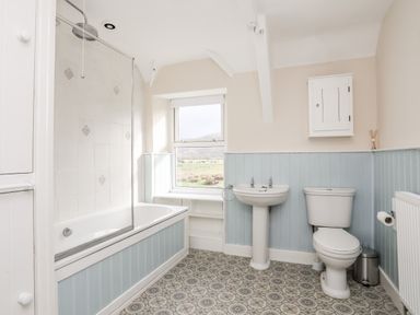 A bathroom with a bathtub shower sink toilet and window at Glyn Morfa in Harlech