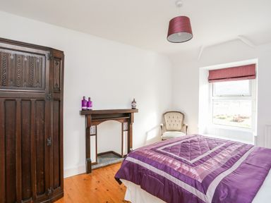 A bedroom with a purple bedspread an armchair wooden floor and a wooden wardrobe at Glyn Morfa in Harlech