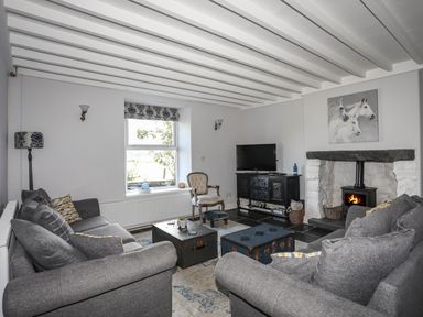 A living room with gray sofas a window a wood burning stove and a television at Glyn Morfa in Harlech