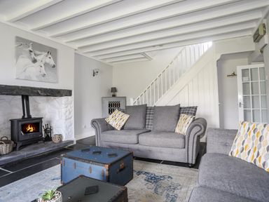 A living room with grey sofas a wood burning stove and a staircase at Glyn Morfa in Harlech