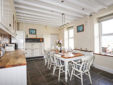A dining room with a wooden table set for six and kitchen cabinets along one wall at Glyn Morfa in Harlech
