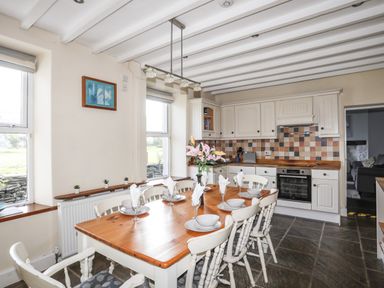 A kitchen with a wooden dining table set with dishes and flowers at Glyn Morfa in Harlech