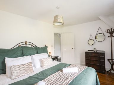 A bedroom with a double bed green bedding bedside table dark wood chest of drawers round mirrors and a coat stand at Glyn Morfa in Harlech
