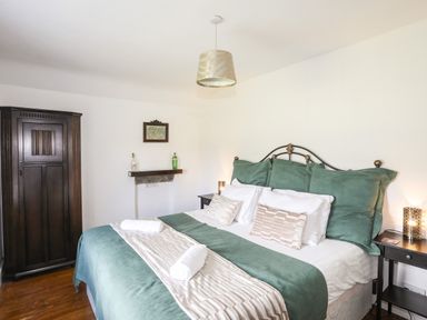 A bedroom with a bed with pillows and blankets a wooden wardrobe and bedside tables with lamps at Glyn Morfa in Harlech