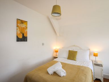 A bedroom with a bed yellow bedding lamps and a yellow flower picture on the wall at Glyn Morfa in Harlech