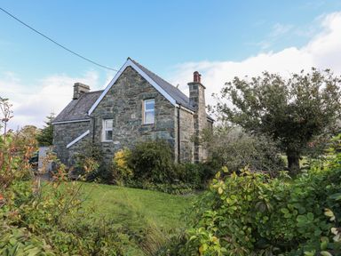 An exterior view of a stone house with a garden and trees at Glyn Morfa in Harlech